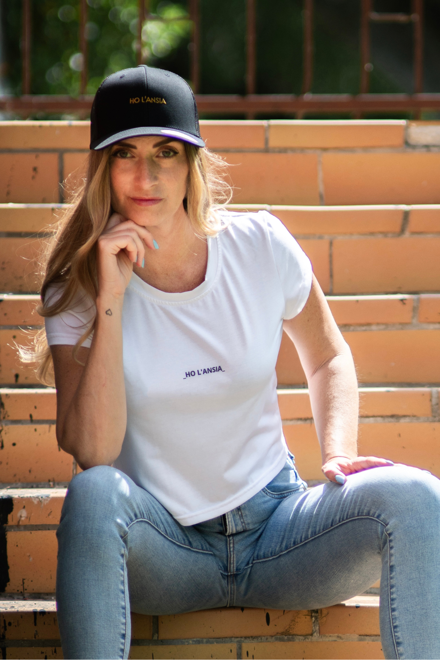 Model wearing Silyp Ho L'Ansia Crop Tee with matching black cap, seated on stairs in daylight