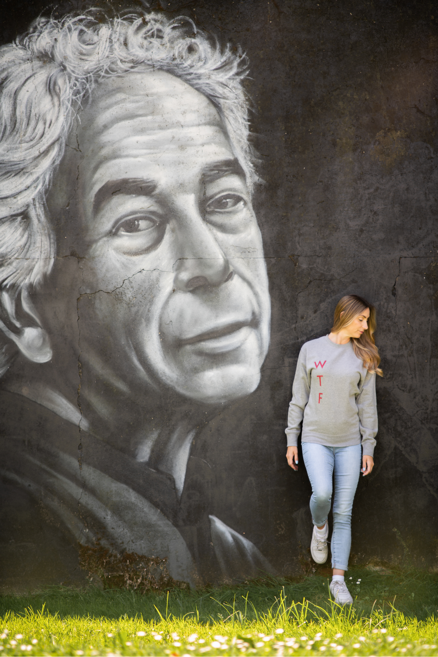 Model wearing grey WTF unisex sweatshirt in front of large black and white graffiti mural