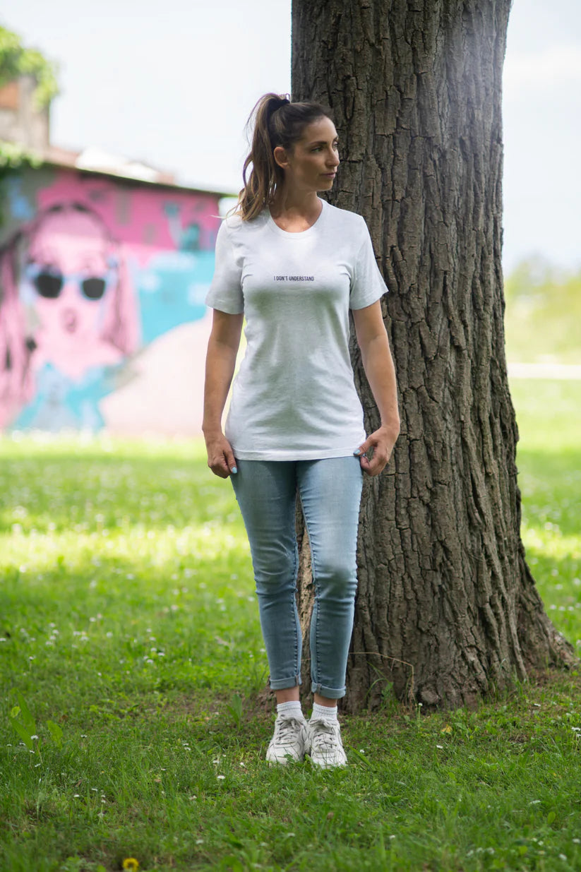 Woman wearing a white t-shirt with a logo, standing next to a tree in an outdoor setting.