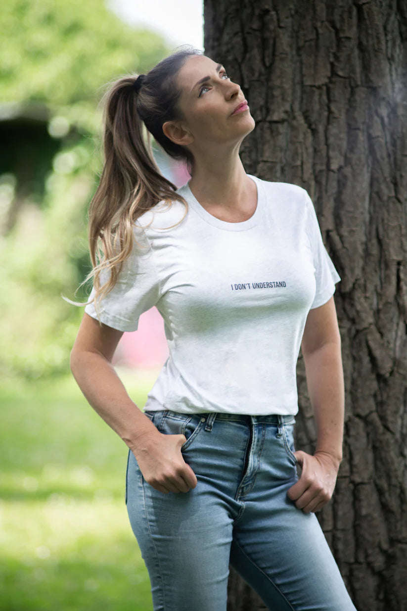Woman wearing a white t-shirt with text and blue jeans standing next to a tree in an outdoor setting.